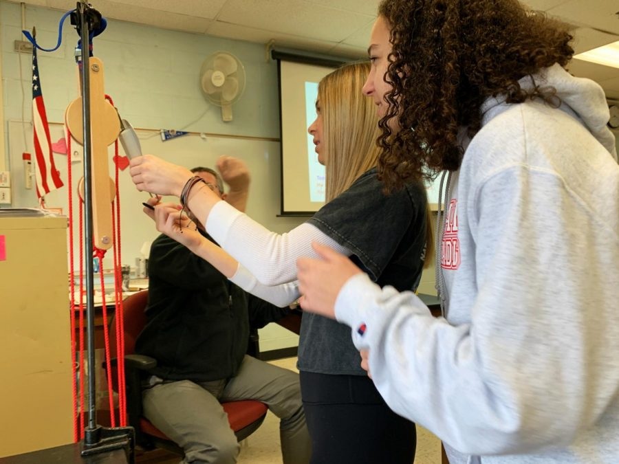 Juniors Elle Gurland and Kathleen Tobia talk with AP Physics teacher Mr. Breig about their energy calculations using a pulley.