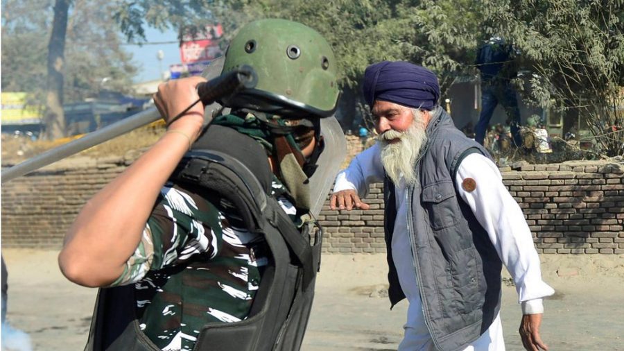 A paramilitary policeman swings his baton at an elderly Sikh man, a photograph that has become the defining image of the ongoing farmers protest in India. 