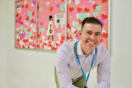 Mr. David Lange stands in front of his student interactive bulletin board, located outside of room 149.