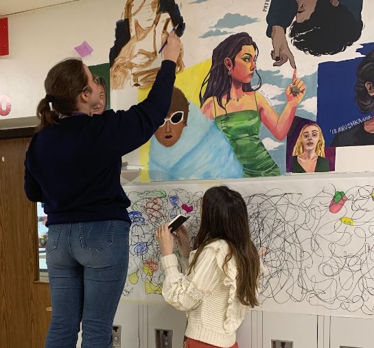 Aleksandra Korza painting a self portrait in the art hallway with the help of Madeline Miller.

